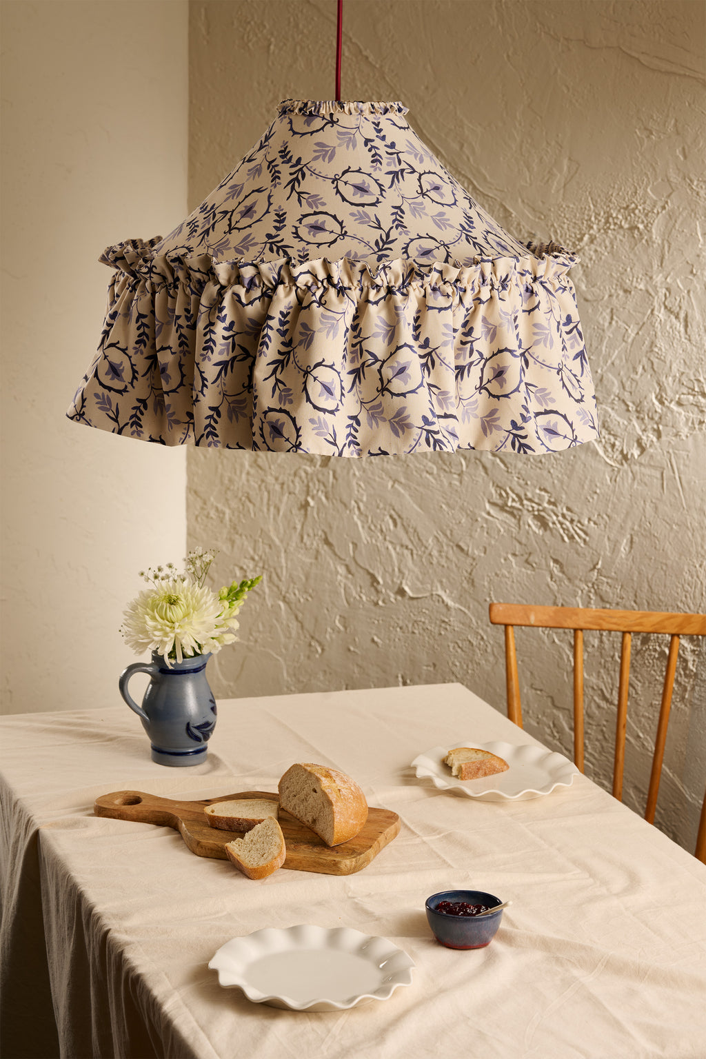 Daunder Ruffle Statement Lampshade in Indigo hanging above a dining table, set against a cream textured wall