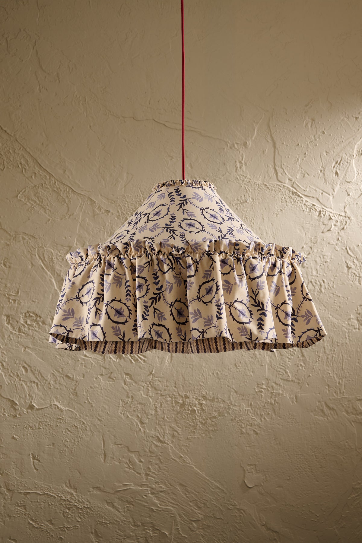Daunder Ruffle Statement Lampshade in Indigo with frilled skirt and contrast lining hanging in front of a textured wall
