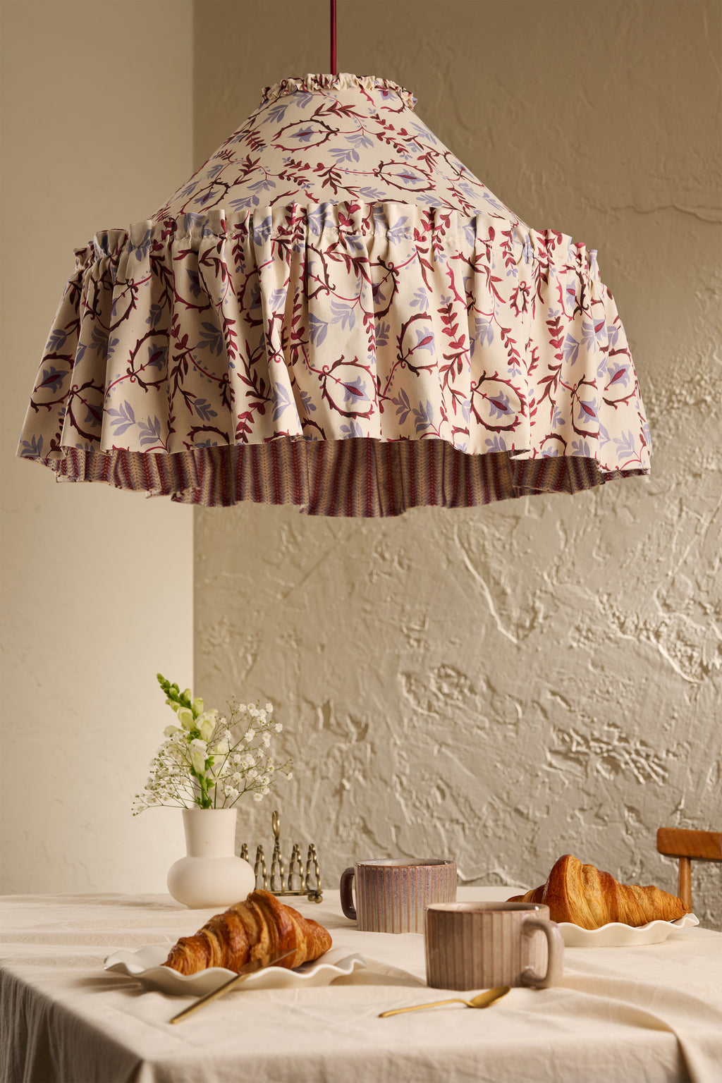 Daunder Ruffle Statement Lampshade in Merlot & Dusty Blue with contrasting stiped lining, hanging above a dining table in a warm neutral interior