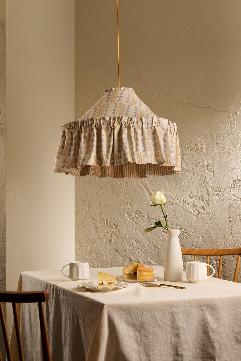 Ellis Ruffle Statement Lampshade in Dusty Sky & Ochre hanging above a dining table, showing the contrasting geometric lining