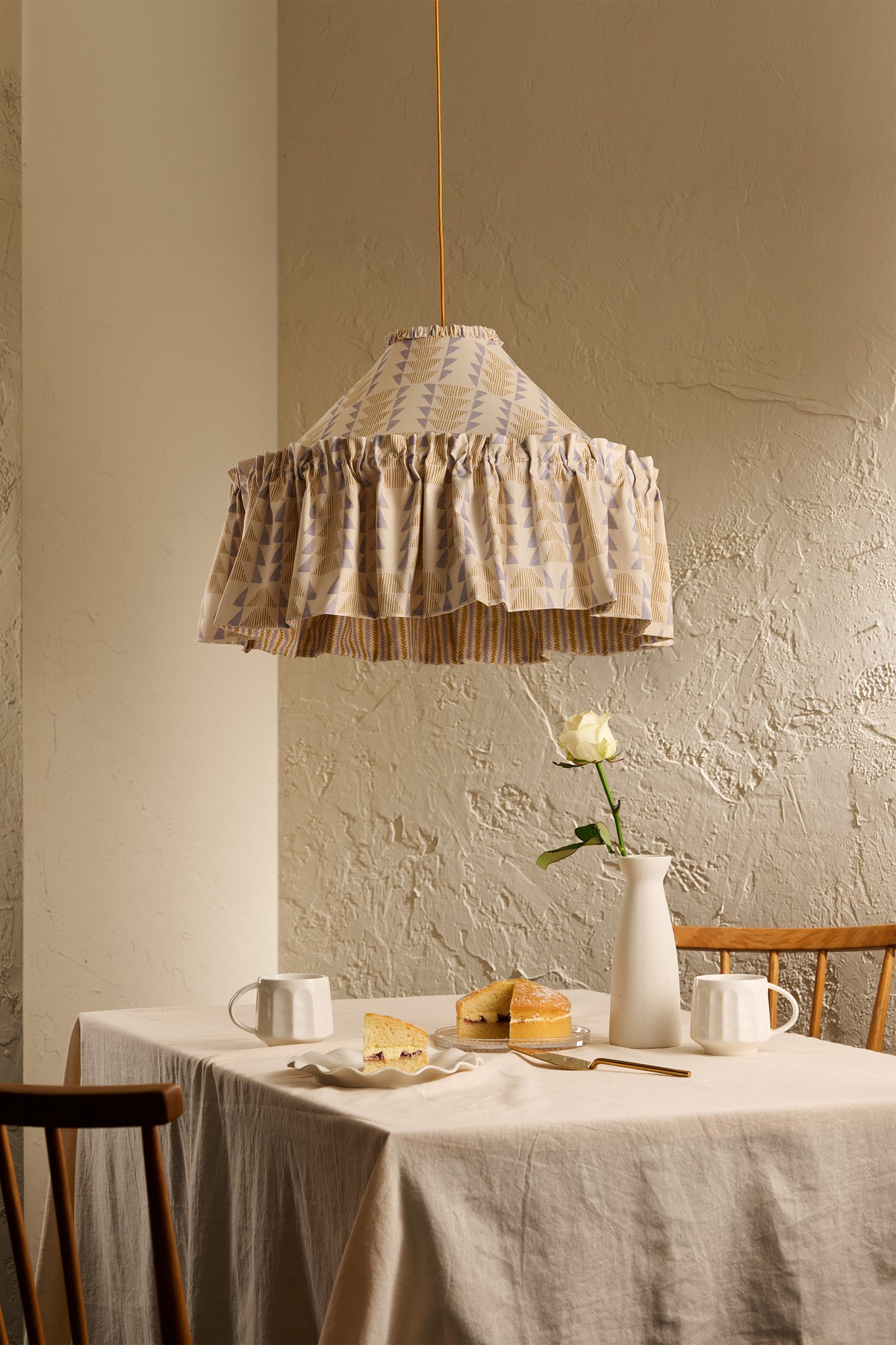 Ellis Ruffle Statement Lampshade in Dusty Sky & Ochre hanging above a dining table, showing the contrasting geometric lining