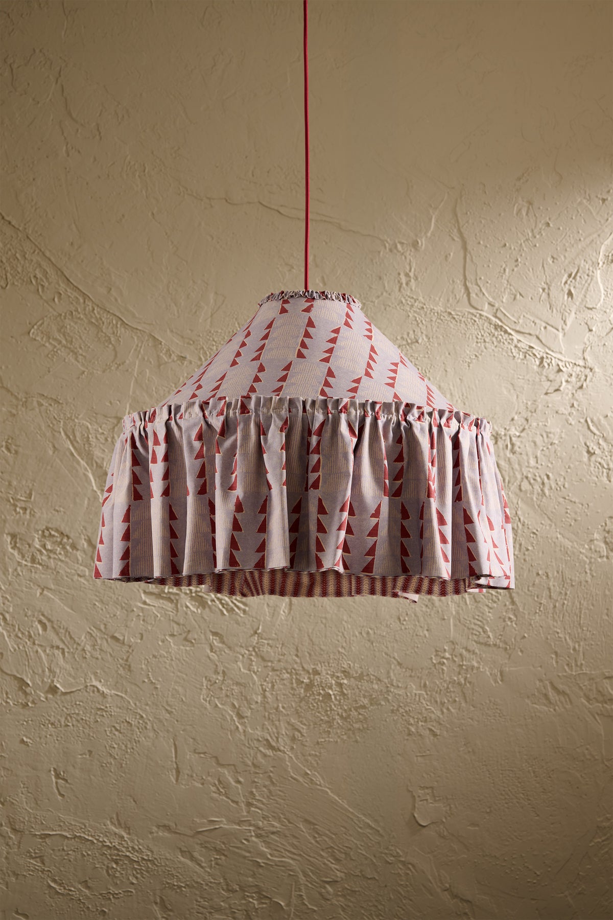 Ellis Ruffle Statement Lampshade in Dusty Blue & Merlot showing the gathered ruffle and contrasting geometric lining hanging in front of a textured wall