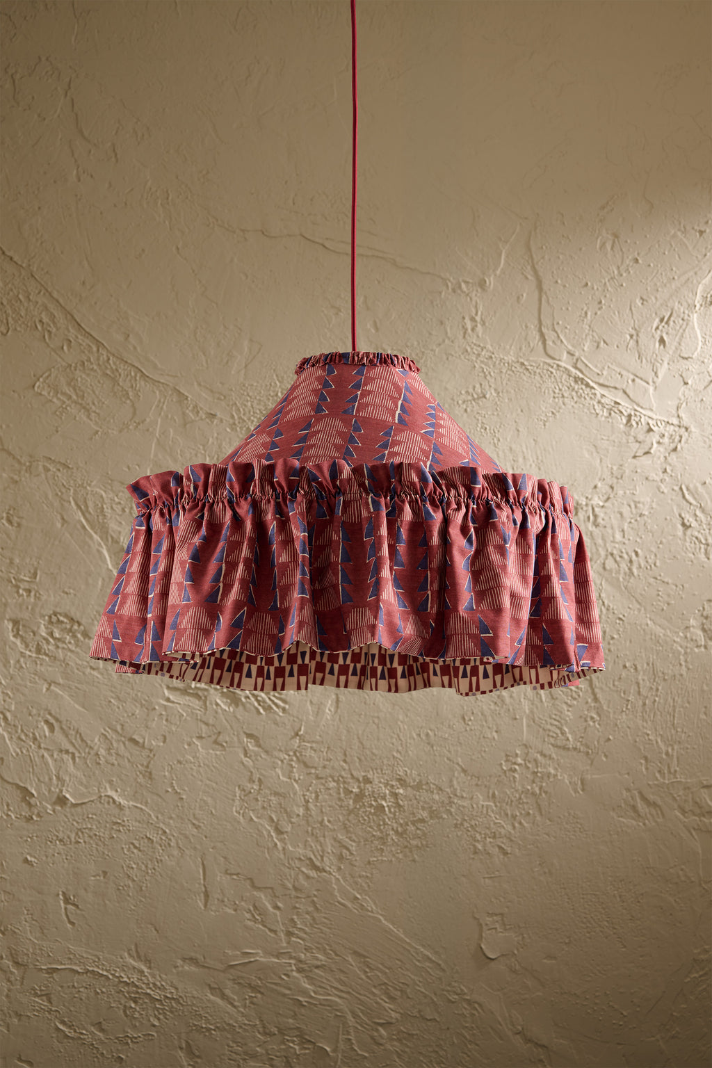 Ellis Ruffle Statement Lampshade in Merlot showing the gathered ruffle and contrasting geometric lining hanging in front of a textured wall