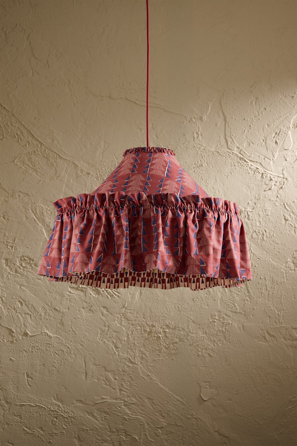 Ellis Ruffle Statement Lampshade in Merlot showing the gathered ruffle and contrasting geometric lining hanging in front of a textured wall