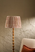 Ellis pleated lampshade in Merlot on a wooden floor lamp beside a cream chair in a warm neutral interior
