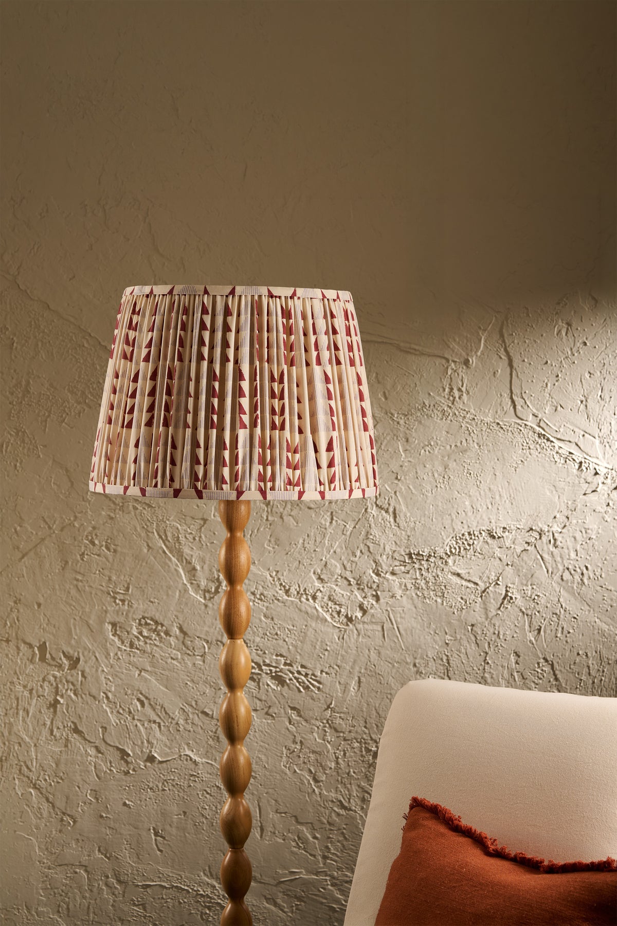 Ellis pleated lampshade in Merlot on a wooden floor lamp beside a cream chair in a warm neutral interior