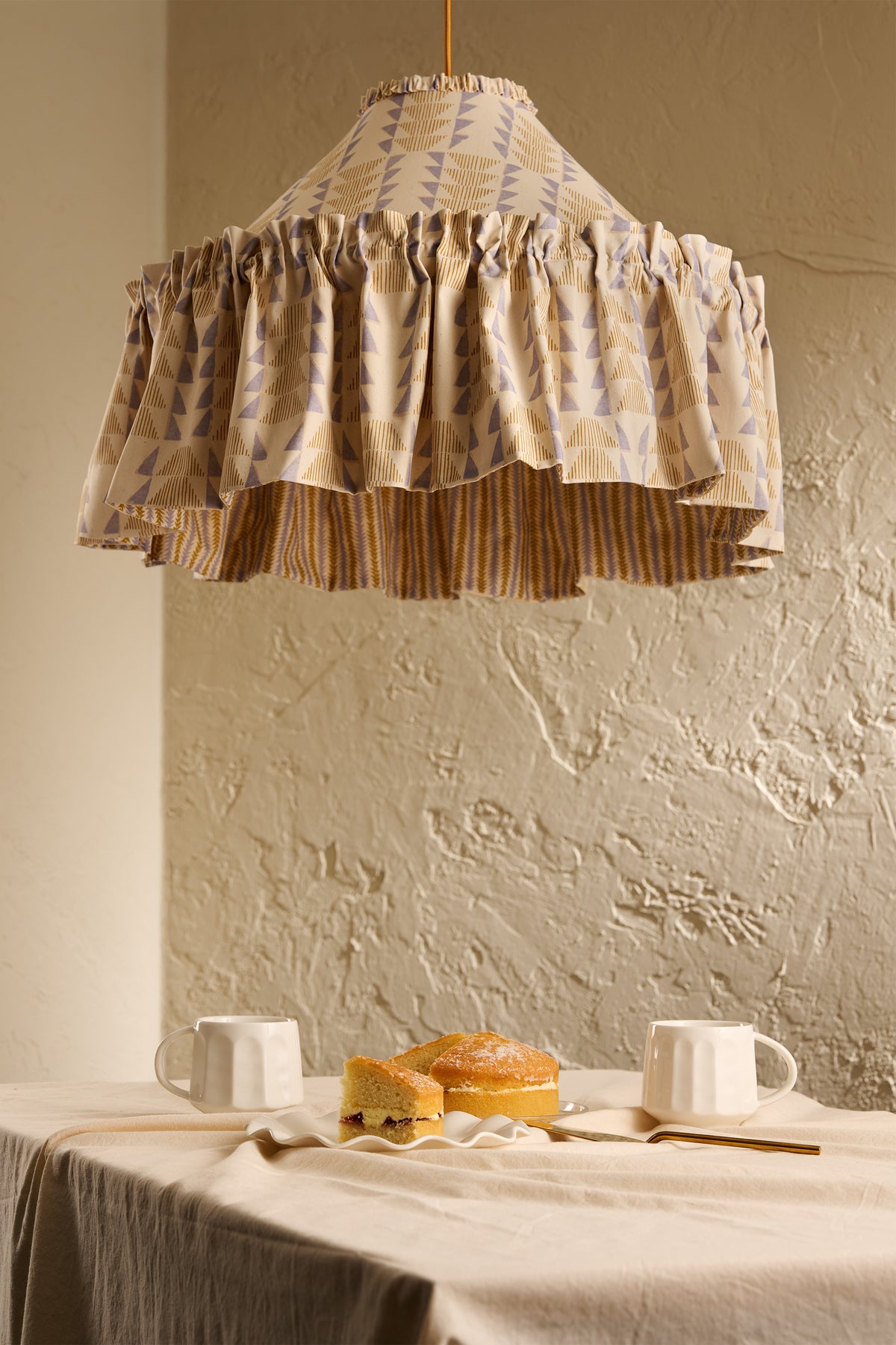 Close-up of Ellis Ruffle Statement Lampshade in Dusty Sky & Ochre showing the gathered ruffle and contrasting geometric lining above a dining table