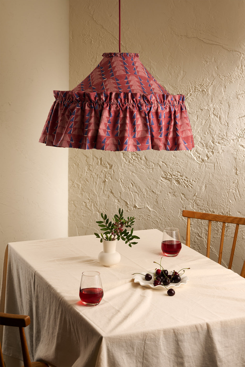 Ellis Ruffle Statement Lampshade in Merlot hanging above a dining table in a warm neutral interior