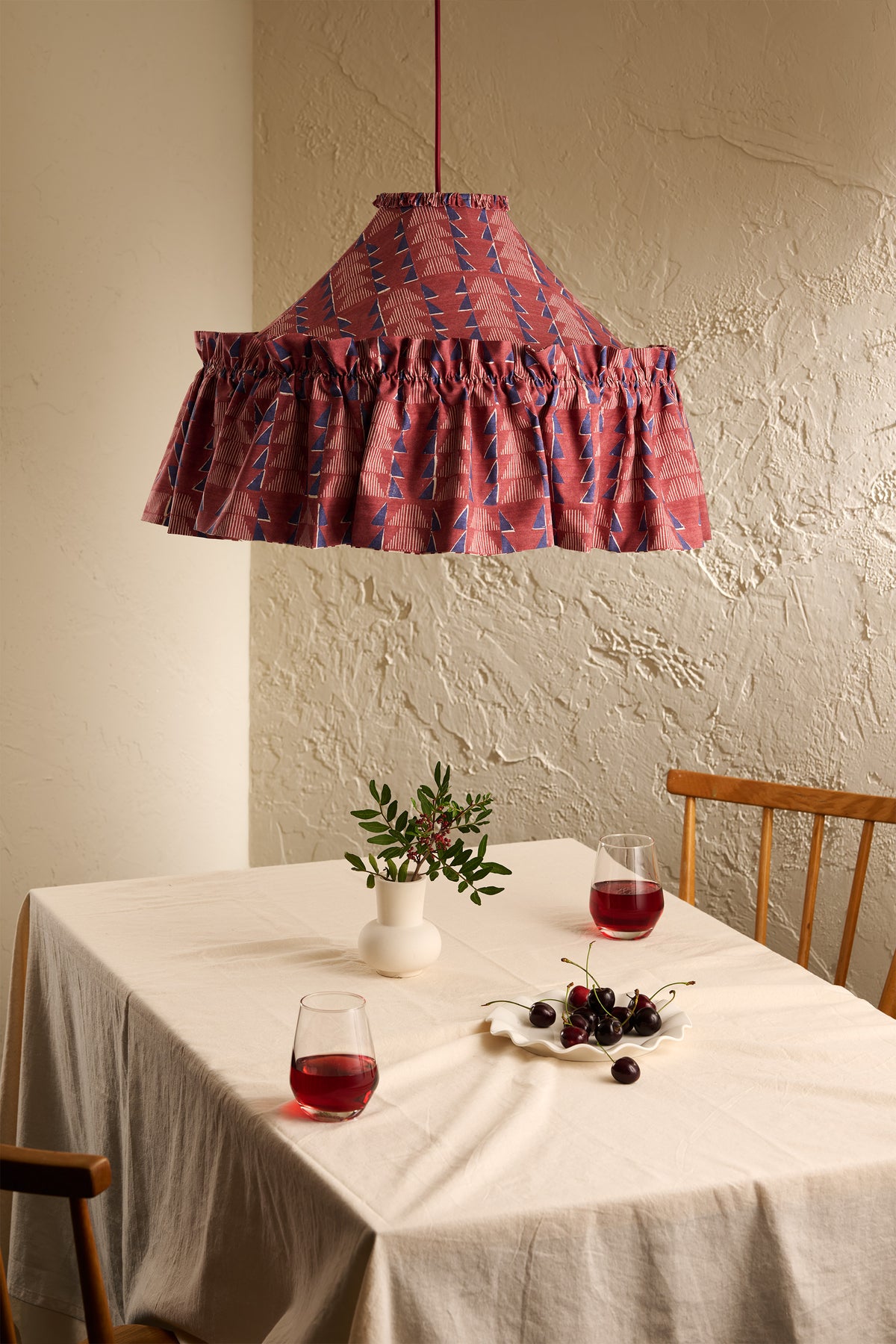 Ellis Ruffle Statement Lampshade in Merlot hanging above a dining table in a warm neutral interior