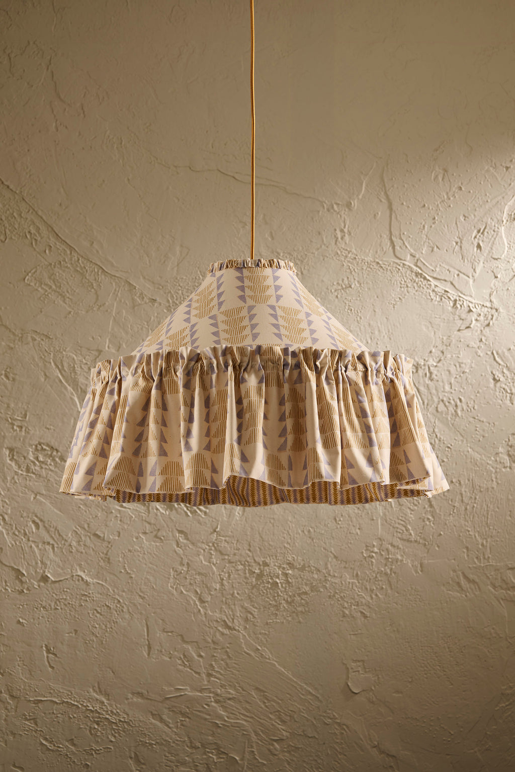 Ellis Ruffle Statement Lampshade in Dusty Sky & Ochre hanging in front of a textured wall showing the contrasting geometric lining