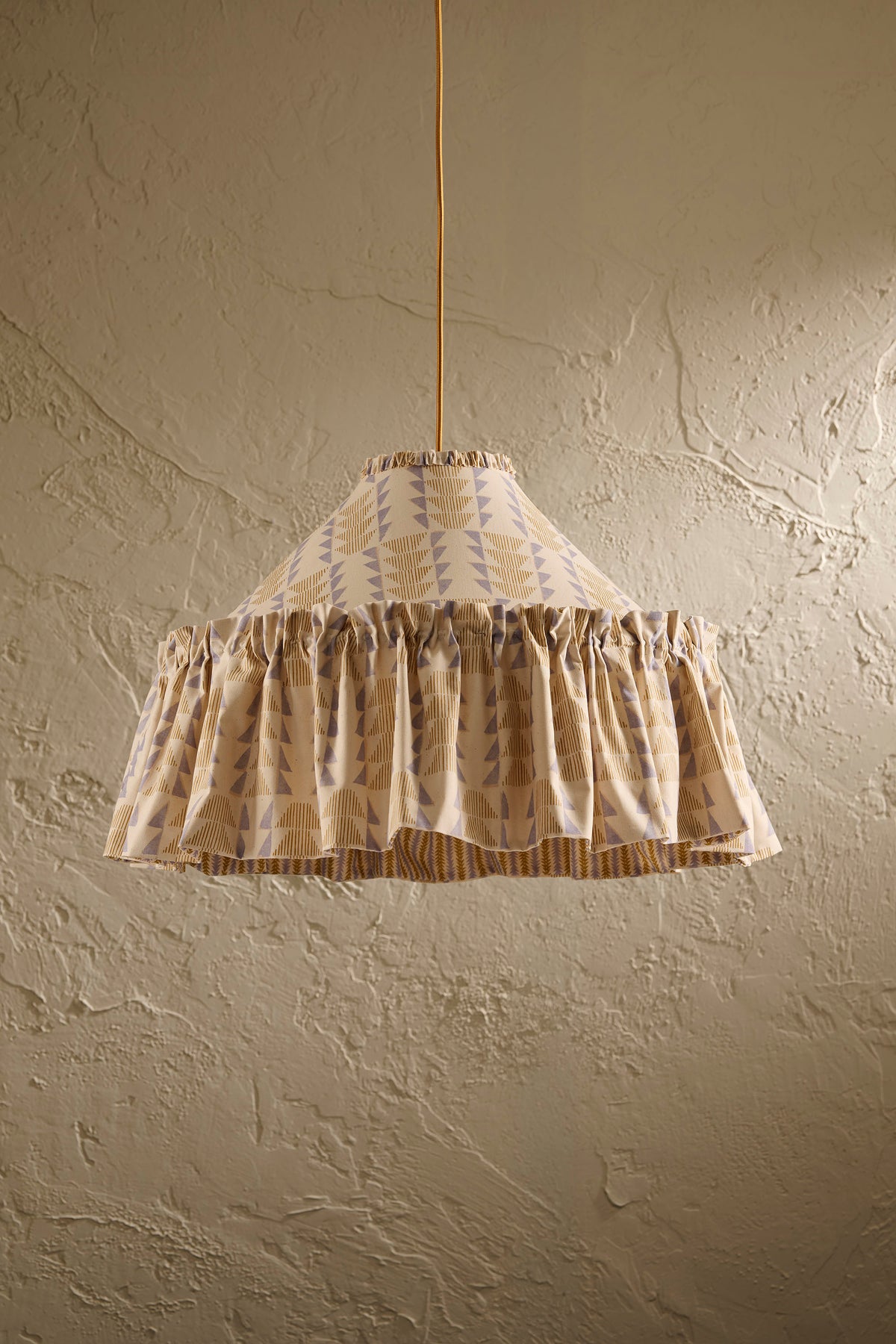 Ellis Ruffle Statement Lampshade in Dusty Sky & Ochre hanging in front of a textured wall showing the contrasting geometric lining